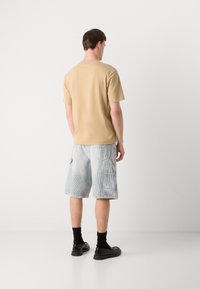 Beige, rövid ujjú póló, amely szürke csíkos cargo rövidnadrággal van párosítva, oldalsó zsebekkel. A modell fekete cipőt és zoknit visel.