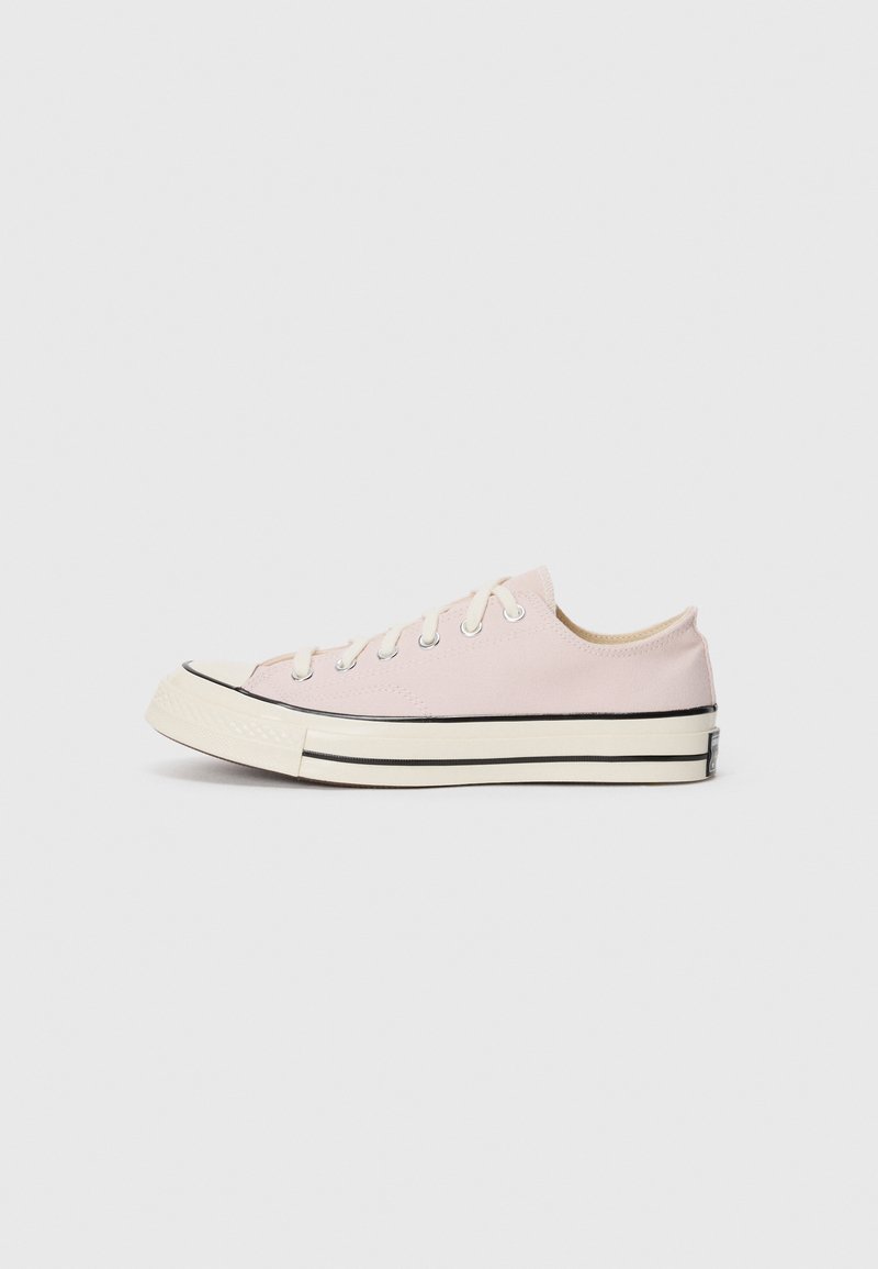 Deportivas de lona rosa claro con puntera redondeada, suela de goma blanca, raya negra y diseño de lazada con cinco ojales. Textura suave, diseño bajo.