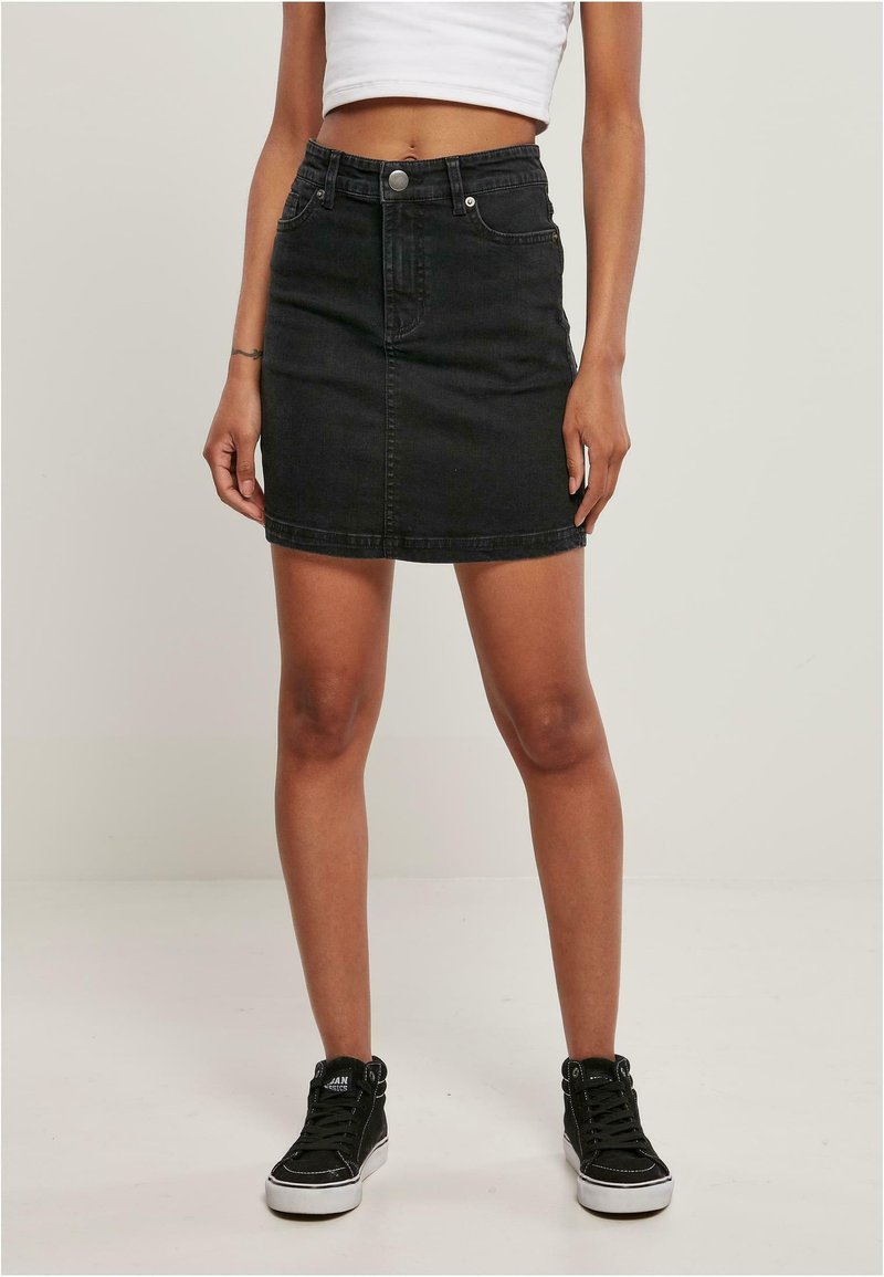 Zwarte denimrok met een aansluitende silhouet, sluiting met knopen aan de voorkant en twee zijzakken. Gecombineerd met zwarte hoge sneakers.