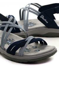Sandali incrociati navy e grigi con sottopiede grigio imbottito, superficie texturizzata, suola in gomma e motivi geometrici sulla soletta.