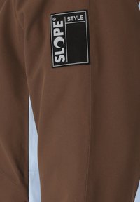 Brauner Oberstoff mit weißem Seitenpanel, das auf der oberen linken Seite ein großes schwarz-weißes „SLOPE STYLE“ Logo-Patch zeigt. Glatte Textur.