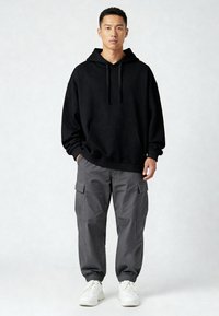 Sudadera negra con capucha y bolsillo frontal, combinada con pantalones cargo grises con bolsillos laterales y puños elásticos, completada con zapatillas blancas.