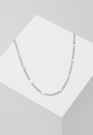 Silberne Kettenanhänger mit ovalen Gliedern und strukturierten runden Akzenten, die ein elegantes und minimalistisches Design auf einem weißen Sockel präsentieren.