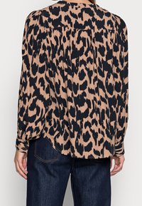 Blusa a stampa leopardo in beige e nero, con vestibilità ampia, maniche lunghe e dettaglio arricciato sul retro. Tessuto morbido con una leggera lucentezza.