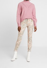 Suéter rosa de punto con textura acanalada y detalles de corte, combinado con pantalones claros de estampado floral y botas blancas de tobillo con tachuelas.
