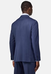 Giacca blu navy esposta da dietro, con una texture liscia, spalle strutturate e dettagli sottili sui polsini.