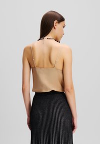 Beige satijnen camisole met dunne verstelbare bandjes, gecombineerd met een zwarte geplooide rok met metallic strepen, gezien vanuit de achterkant.