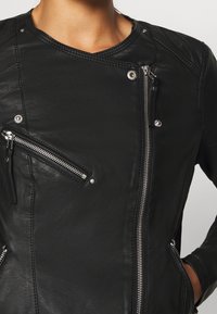 Giubbotto in pelle nera con un design aderente, dotato di più cerniere, dettagli in argento e un tessuto testurizzato per un ulteriore tocco di stile.