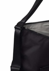 Sac d'épaule en tissu noir avec sangle réglable et fermeture éclair partiellement ouverte révélant une doublure intérieure grise.