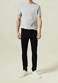 Šedé tričko s krátkým rukávem, černé úzké džíny a bílé tenisky; minimalistický design s čistými liniemi a bez viditelných vzorů či log.