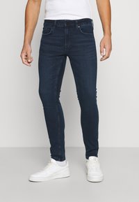 Jeans skinny de un azul oscuro, fabricados en denim, con un diseño clásico de cinco bolsillos, cierre con botón y una textura sutilmente desgastada.