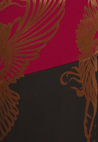 Tissu rouge et noir avec motifs abstraits floraux et plumes en cuivre métallique chevauchant les deux blocs de couleur.