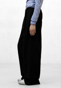 Pantalones negros anchos hechos de un material suave, con una cintura alta y un corte relajado, combinados con zapatillas blancas y una blusa de manga larga azul.