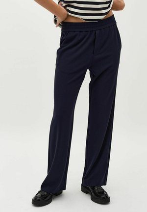Navy blue, lightweight trousers with an elastic waistband, side pockets, and a relaxed fit. Worn with black loafers on a neutral background.