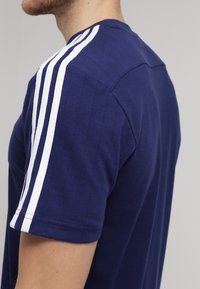 Granatowy bawełniany t-shirt z białymi paskami na ramionach i prążkowaną fakturą. Projekt zawiera okrągły dekolt i krótkie rękawy.