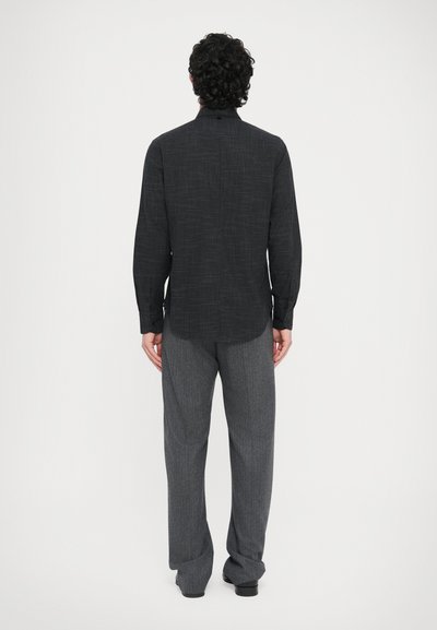 Sort langærmet skjorte med tekstureret mønster, kombineret med grå teksturerede bukser set bagfra. Begge beklædningsgenstande har en løs pasform.