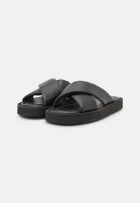 Infradito in pelle nera con ampie cinture sovrapposte e una suola spessa e texturizzata. Presentano una finitura liscia e un design con punta aperta.