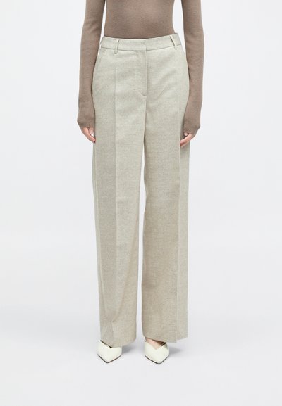 Svijetlosmeđe široke hlače izrađene od teksturirane tkanine, s ravnim prednjim dijelom, bočnim džepovima i uparenim s bijelim cipelama na špic.