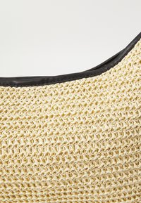 Sac en paille tissé avec un corps beige clair et des bordures en cuir noir le long du bord supérieur, présentant un motif texturé et une forme incurvée.