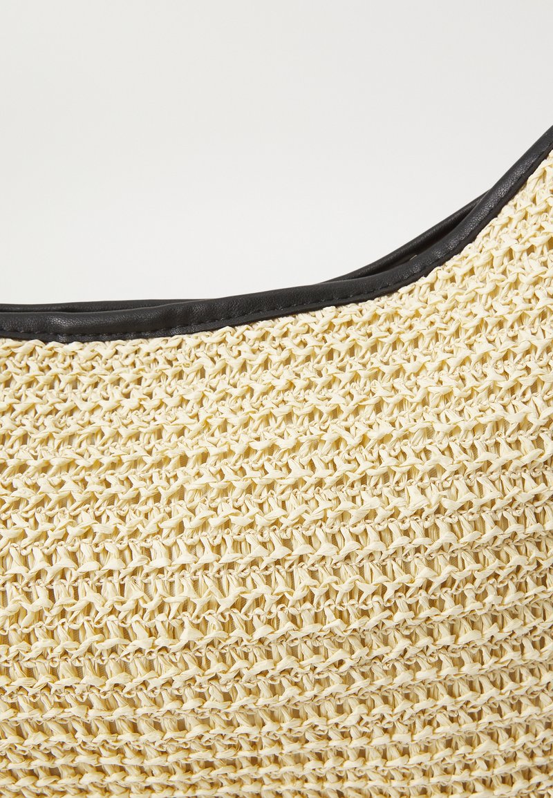 Bolso de paja tejido con un cuerpo de color beige claro y ribete de cuero negro en el borde superior, con un patrón texturizado y forma curva.