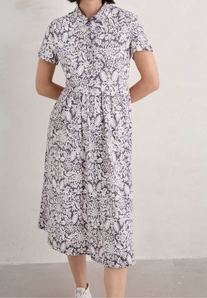 Kortærmet kjole i lilla stof med hvide blomstermønstre, med knaplukning fortil og samlet talje, som falder til midt på læggen.