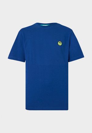 T-shirt bleu à manches courtes avec un petit écusson jaune représentant une empreinte de patte noire à trois doigts et un visage avec des crocs sur le côté gauche de la poitrine.