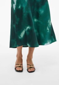 Robe en satin vert au design fluide avec une fente sur le côté, associée à des sandales noires à lanières avec un accent en métal doré.