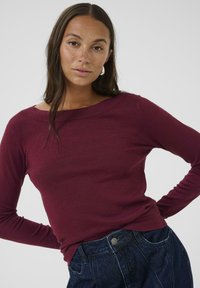 Bordeaux lange mouw top met een wijde halslijn, gestructureerde stof en een getailleerde silhouet, gecombineerd met donkerdenim high-waisted jeans.