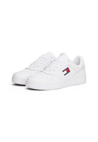 Paire de baskets basses blanches avec lacets et écusson logo Tommy Jeans sur le côté, présentées sur un fond blanc.