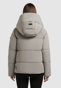 Puffjakke i lys grå med stor hætte, quiltet design, sidelommer og logodetail på nederste venstre side.