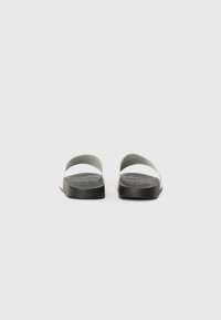 Sorte og hvide slidesandaler med flad sål og rundt, åbent design. Overdelen har bløde, brede stropper for komfort. Tekstureret indersål.