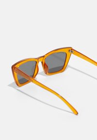 Oranžno prozorne mačje oči sončna očala s sivojimi lečami in ravnimi kraki. Jasna teksturirana obdelava in minimalistična zasnova.