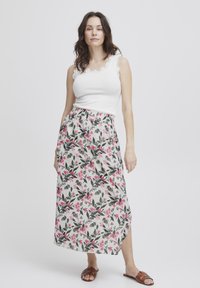 Jupe maxi florale avec une base blanche, ornée de fleurs roses et de feuilles vertes. Taille élastique et fente latérale. Associée à un débardeur blanc.