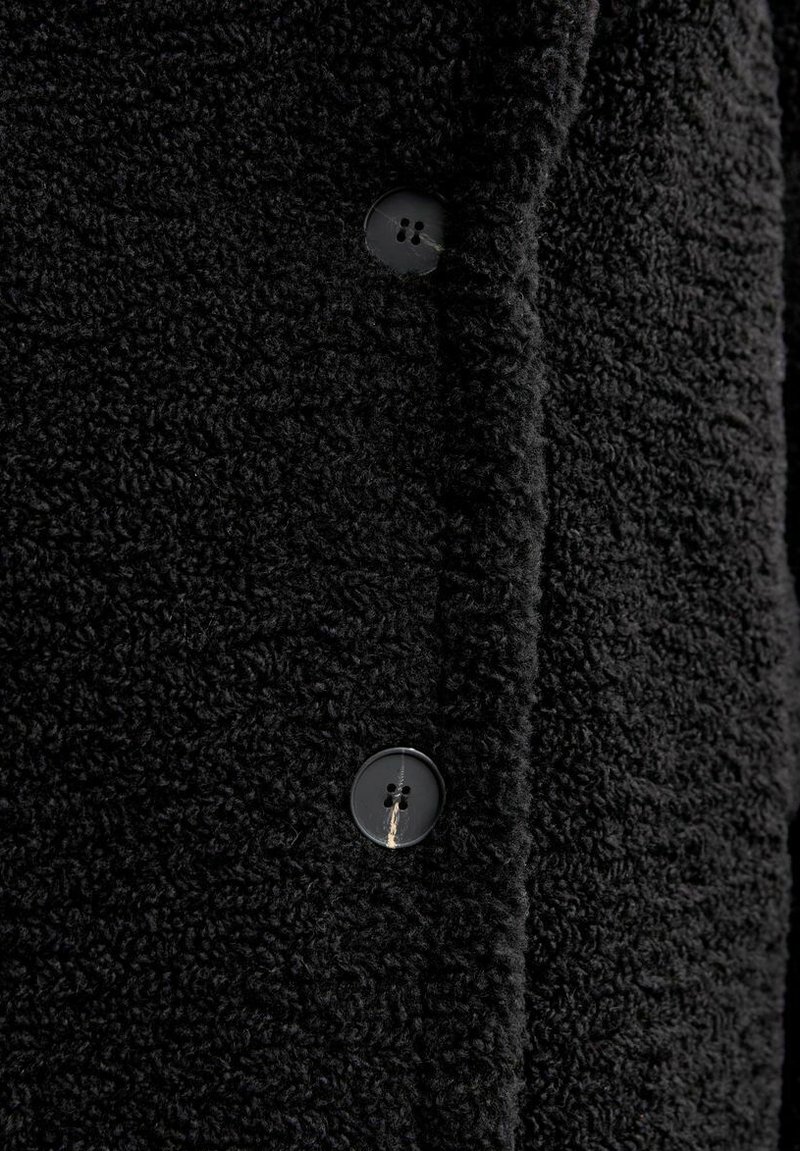 Czarna polarowa tkanina o teksturowanej powierzchni; posiada czarny guzik z czterema otworami wzdłuż plisowania, podkreślając miękki, ciepły design.