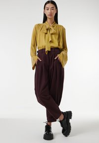 Blusa de satén amarilla con cuello de lazo, combinada con pantalones holgados burdeos y zapatos negros de suela gruesa con cordones.