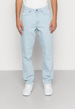 Jeans de denim azul claro com corte reto, design de cinco bolsos e detalhes de costura visíveis. Combinados com ténis brancos.
