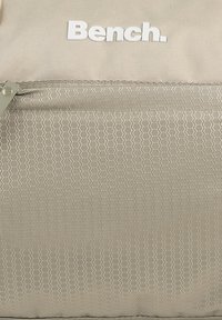 Beige rugzak met een hexagonaal patroon op het voorvak. Voorzien van een ritsafsluiting en een wit "Bench." logo aan de bovenkant. Gemaakt van duurzaam materiaal.
