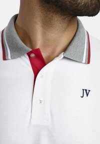 Weißes Polohemd mit grauem Kragen und roten Akzenten, mit einer Drei-Knopf-Leiste und einem gestickten "JV"-Logo in Marineblau.