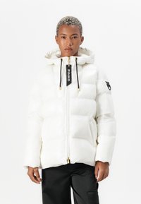 Giacca a vento bianca con finitura lucida, cappuccio e chiusura zip. Presenta lacci neri e un'etichetta con logo, con tasche laterali.