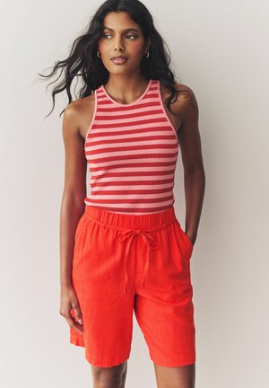 Débardeur rayé rouge et rose associé à un short rouge ample avec une taille élastique et un cordon de serrage ajustable, doté de poches.