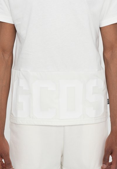 Camicia bianca a maniche corte con orlo traslucido e grande scritta in rilievo "GCDS" in bianco. Realizzata in morbido cotone.