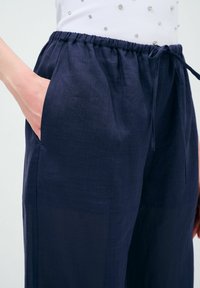 Donkerblauwe linnen broek met een elastische tailleband, trekkoord en zijzakken. De stof lijkt lichtgewicht met een gladde textuur.