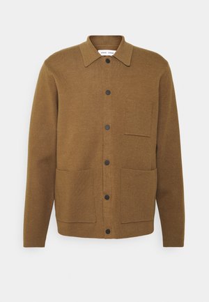 Brun knappet jakke med krave, to forlommer nederst, én brystlomme og lange ærmer på en ensfarvet baggrund.