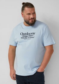 Lichtblauwe katoenen t-shirt met een zwarte grafische tekstprint met de tekst "Buitenleven Gevoel Vooruit! Abonneer Je Op De Natuur." Korte mouwen, ronde hals.