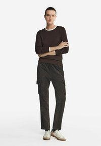 Brun långärmad topp med vit krage, i kombination med mörka cargobyxor med sidofickor och vita sneakers med beige detaljer.