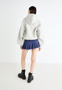 Grey cropped hoodie with a large hood, paired with a blue flared mini skirt and black lace-up boots with chunky soles. Smooth texture overall.