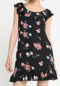 Černé květinové šaty s volánkovým výstřihem a rukávy, zdobené růžemi v bílé a růžové barvě, s volánkovým lemem. Lehce látková textura.