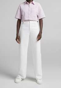 Lila och vit rutad kortärmad tröja, parat med högtalande vita raka jeans och vita sneakers.