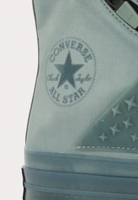 Tênis Converse azul claro com um logo circular contendo uma estrela, tecido suave, sola de borracha e detalhes em estrela texturizados.