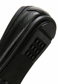 Chaussure en cuir noir avec surface texturée, bout arrondi lisse et semelle en caoutchouc dotée d'un motif antidérapant et de petits points en relief pour l'adhérence.